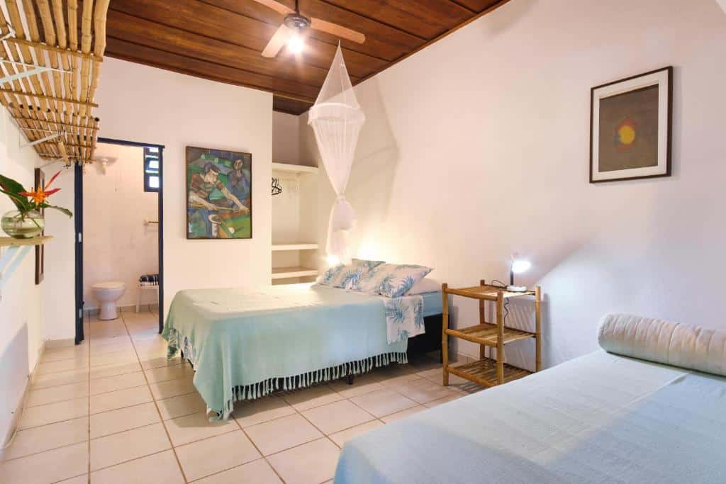 Quarto no Residence Picinguaba, uma cama de casal e uma de solteiro, local amplo, um banheiro, um armário aberto, alguns enfeites rústicos, para representar airbnb em Ubatuba