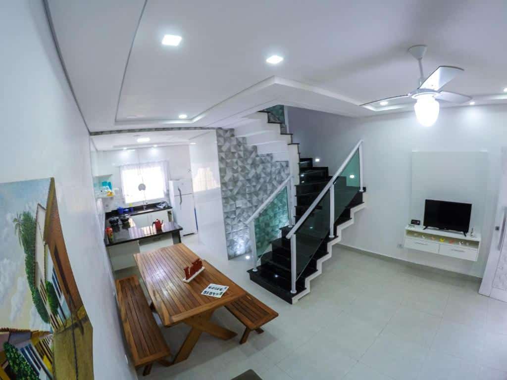 Sala de estar e cozinha da Residencial Maia, com uma escada para o segundo andar, uma mesa com bancos, televisão e uma cozinha, local novo