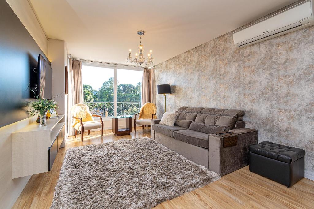 Sala do Rosa Apartamento Giovani Pizetta, com sofá reclinável cinza, poltronas, puff preto, TV e varanda com vista para a natureza