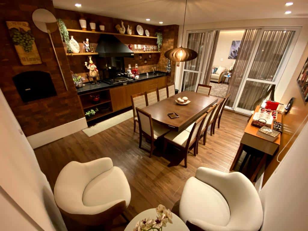 Sala de estar do Apartamento em Campos do Jordão ao lado do Capivari, local amplo e decorado, uma sacada que leva para um segundo ambiente, uma pequena cozinha, uma mesa com dez lugares, tudo com detalhes em madeira