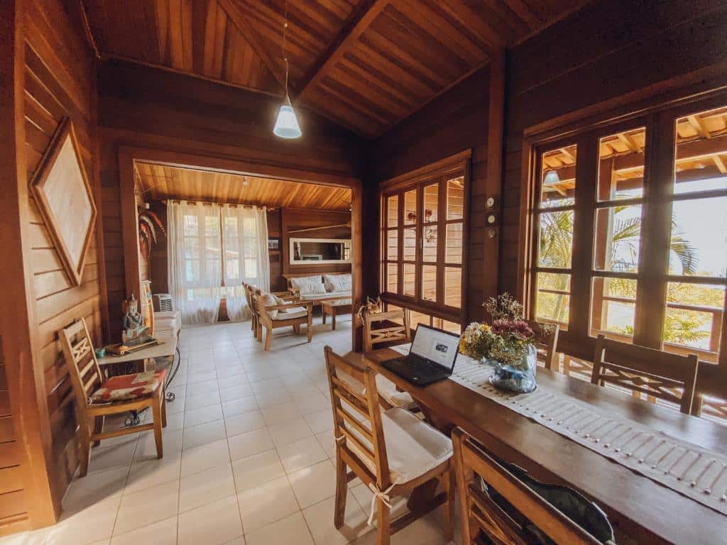 Sala da Casa Ubatuba Vista para o Mar, cercada por janelas, tudo feito em madeira, mesas, cadeiras e ambiente amplo, para representar airbnb em Ubatuba