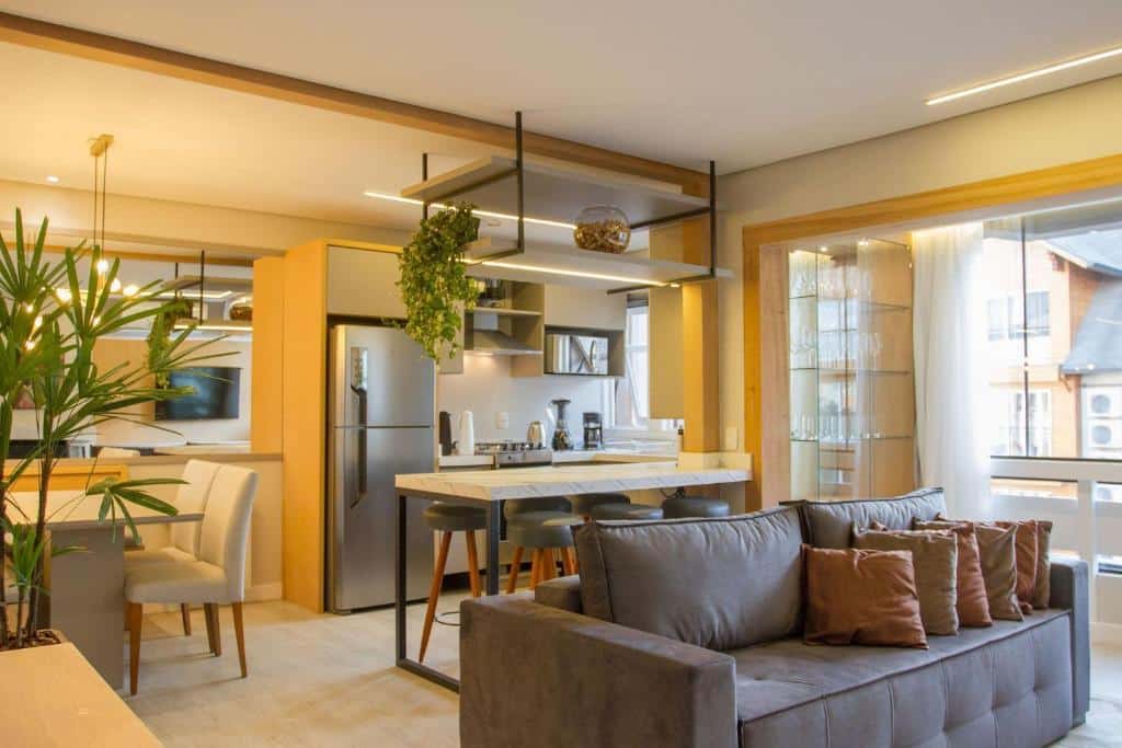 Sala de estar do Incrível apartamento no Centro de Gramado , decoração minimalista, algunas plantas, um balcão com seis lugares, uma mesa com quatro lugares, uma sofá com almofadas e uma sacada envidraçada