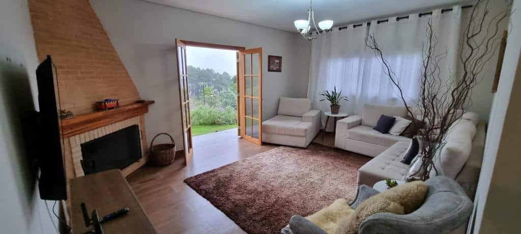 Sala de estar no Refugio em Campos, uma sacada de frente para o gramado, local amplo, uma lareira, uma tapete, alguns sofás e decoração simples