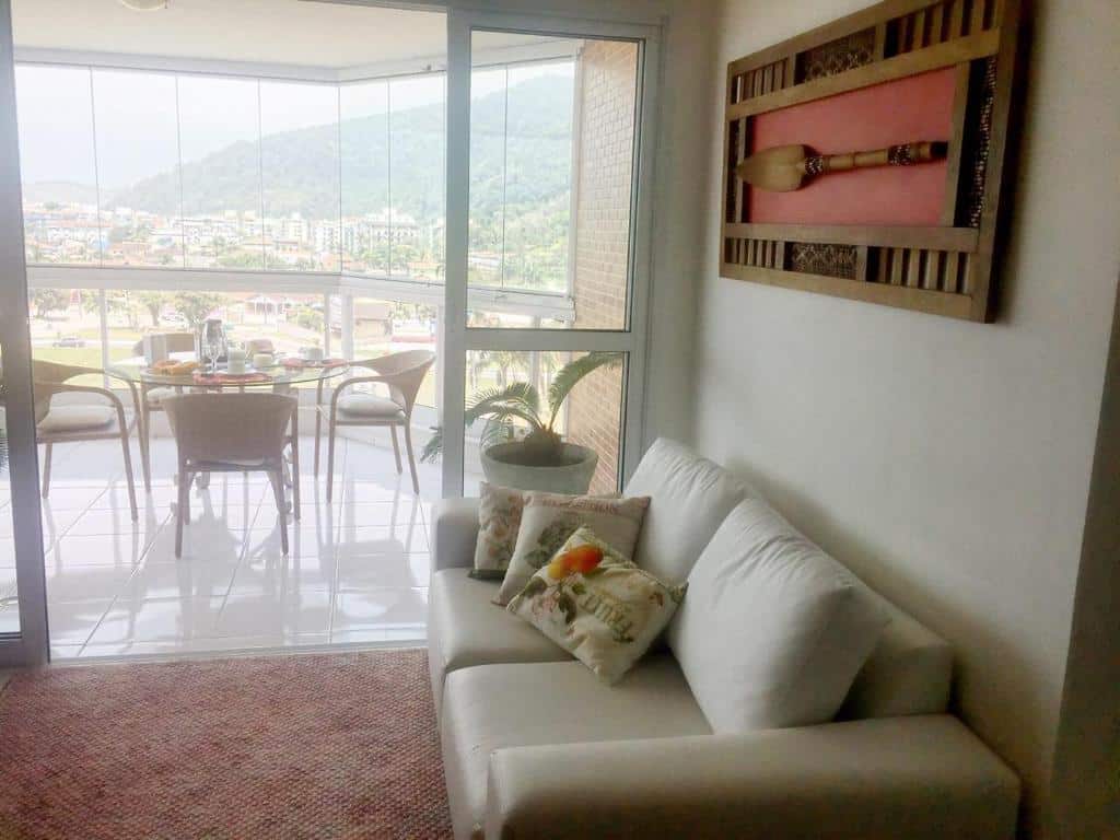Vista da sala e sacada do UBATUBA, APARTAMENTO TOP, um sofá, um quadro, um vaso de plantas e uma mesa com cadeiras na varanda, para representar pousadas na Praia do Tenório