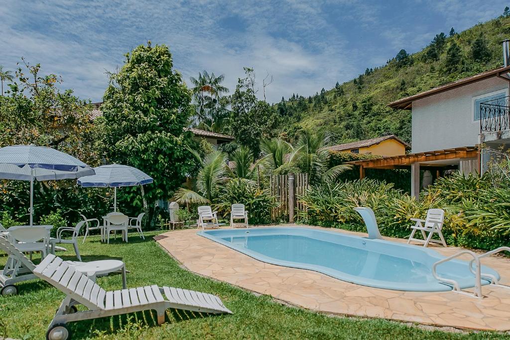 Vista da piscina em Villa Divina Pietra - Ubatuba, uma piscina cercada por um jardim, espreguiçadeiras e as montanhas ao fundo para representar airbnb na Praia das Toninhas em Ubatuba