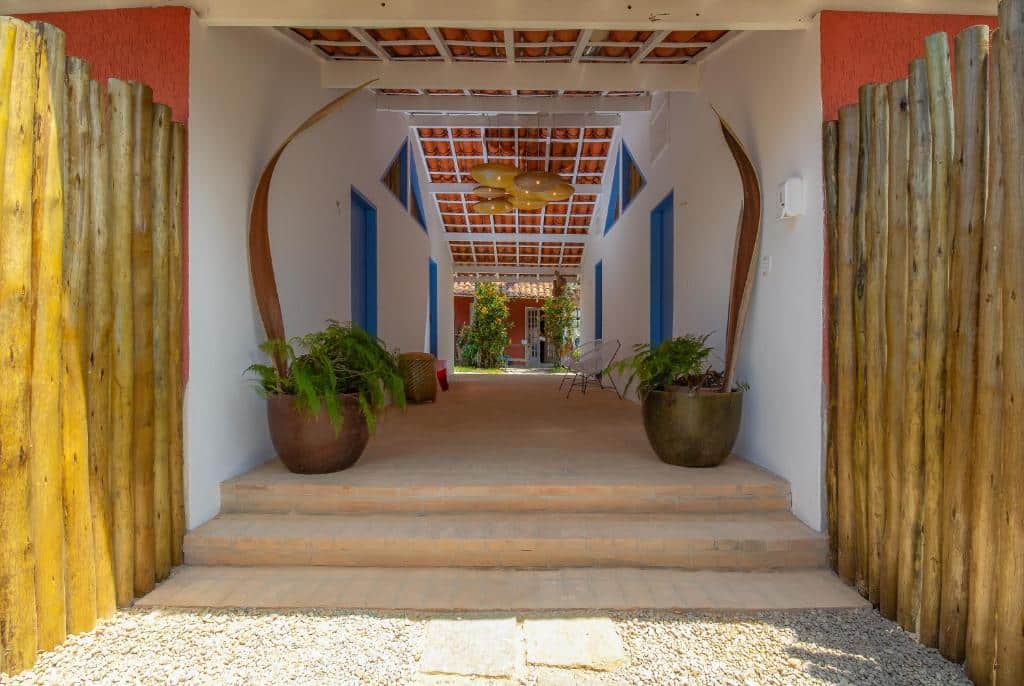 Entrada da  Villa Tennis, local arejado, amplo e rústico, com muitos vasos de plantas, porta de bambu, um pequeno jardim e iluminação com lustres de bambu