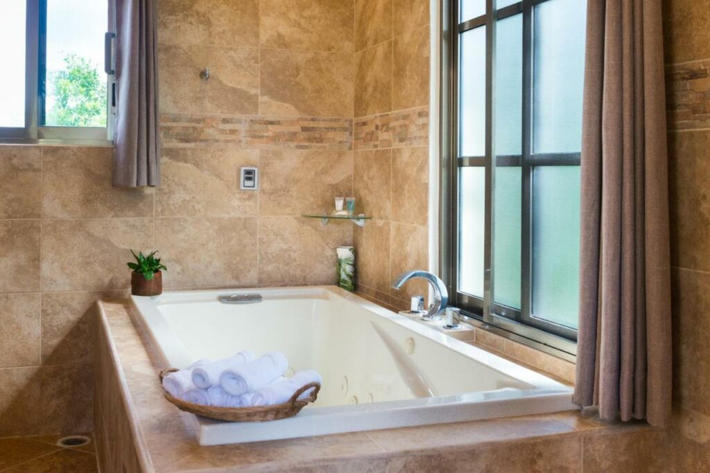 Banheira do Álamos Inn Hotel con Jacuzzi y Piscina com toalhas ao dispor, uma janela e um vaso de flor