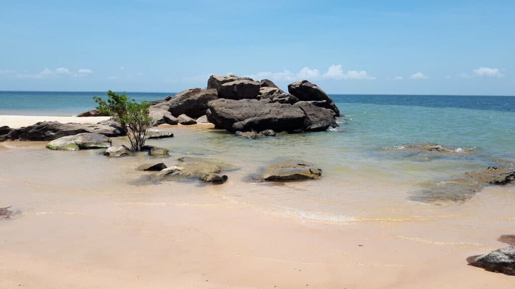 Uma praia com águas transparentes e algumas rochas próximas da areia