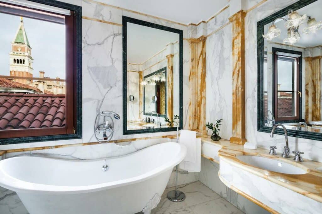 Banheiro inteiro em mármore e com uma banheira, muitos espelhos e uma vista para a cidade no Baglioni Hotel Luna, para representar hotéis em Veneza