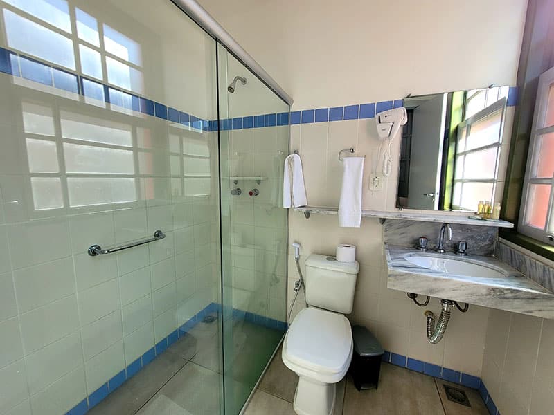 banheiro da pousada dos ofícios com um box amplo, um vaso sanitário e uma pia com espelho
