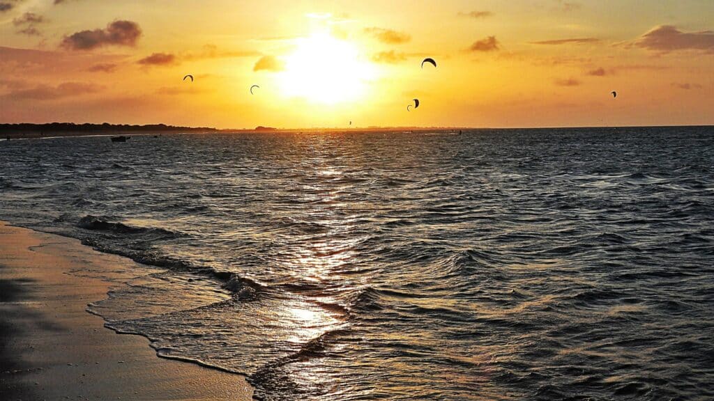 Pôr do sol na praia com ondas suaves, pipas no céu e um brilho dourado refletindo na água e na areia. Essa é uma praia de Barra Grande, um dos melhores lugares para curtir o Réveillon no Brasil.