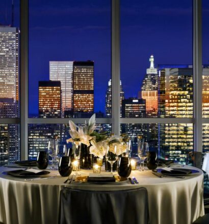 restaurante do Bisha Hotel Toronto com uma ampla janela ao lado com vista para a cidade iluminada de noite