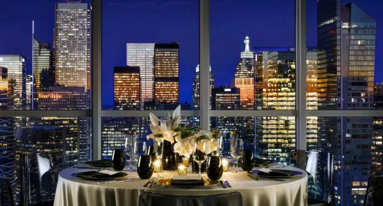 restaurante do Bisha Hotel Toronto com uma ampla janela ao lado com vista para a cidade iluminada de noite