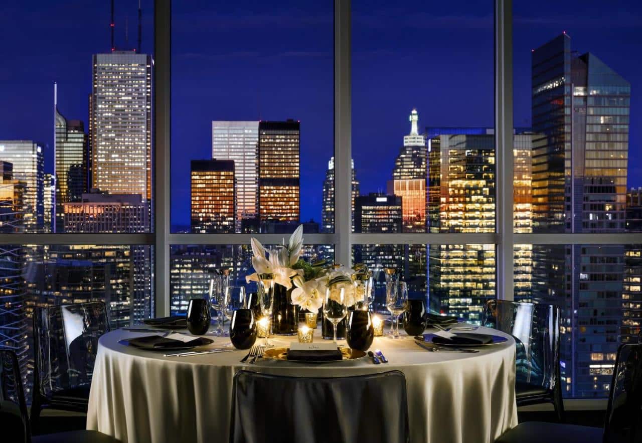 restaurante do Bisha Hotel Toronto com uma ampla janela ao lado com vista para a cidade iluminada de noite