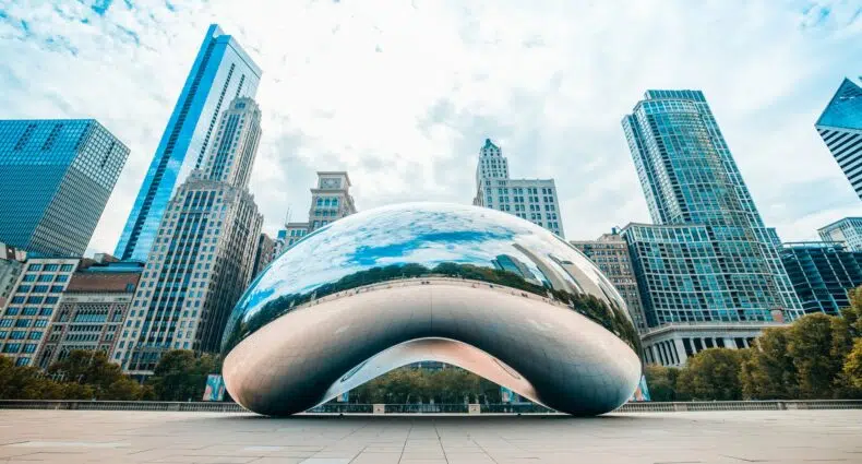 Escultura cloud gate em chicago durante o dia com prédios e árvores atrás ilustrando o post de seguro viagem chicago