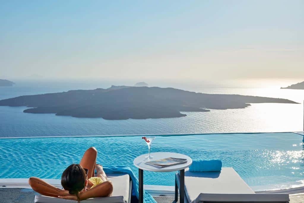 Mulher deitada na beira da piscina do hotel Cosmopolitan Suites, olhando para a Caldeira, em Santorini