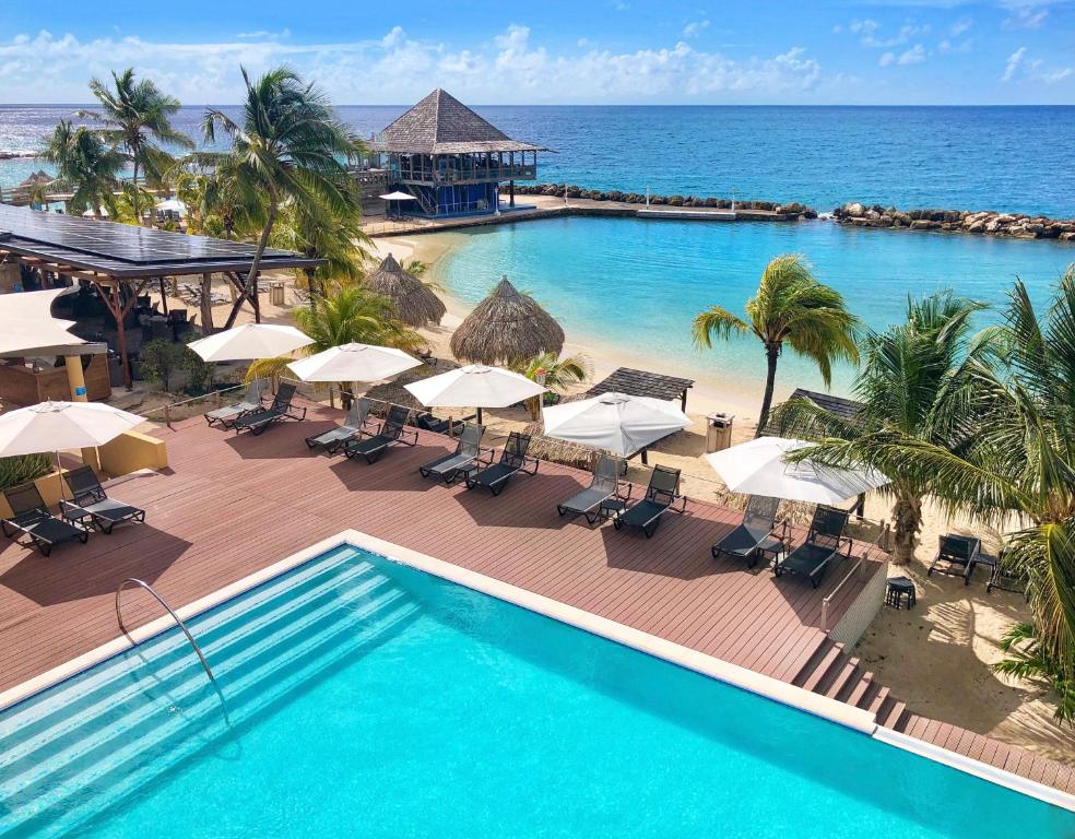 piscina do Curacao Avila Beach Hotel com deque de madeira separado do mar por uma estreita faixa de areia e uma bela vista do oceano