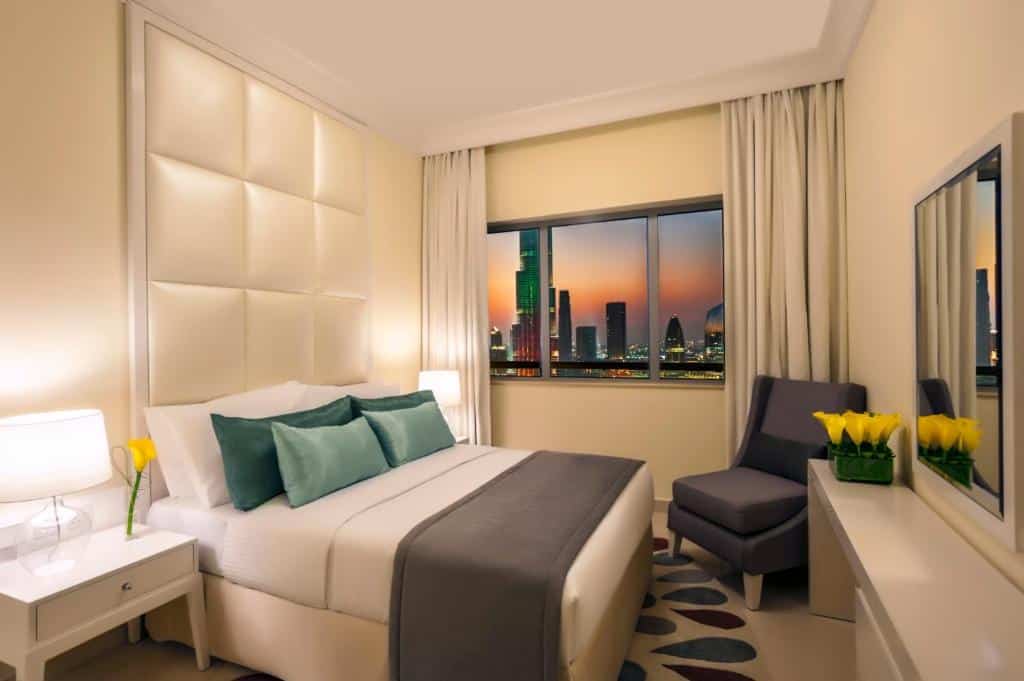 Quarto do DAMAC Maison Dubai Mall Street, com 1 cama de casal, poltrona e janela com vista da cidade e pôr do sol