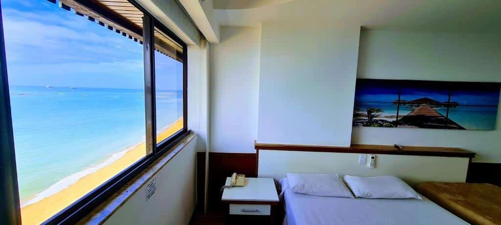 Quarto no  Flat Pasárgada 906 com a janela dando vista direta para a praia, com uma cama de casal e uma de solteiro