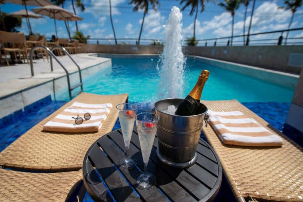 Piscina do Hardman Praia Hotel com espreguiçadeiras e uma mesa com champanhe e taças