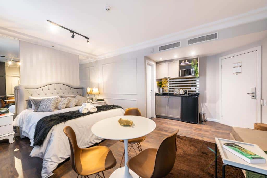 Mesa com três cadeiras, cama grande e pequena cozinha do Higienópolis Sofisticação e Serviços, um dos airbnb em São Paulo