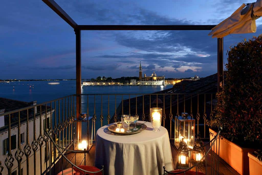 Terraço do Hotel Metropole Venezia com vista para o mar, com uma mesa redonda com velas e taças e duas cadeiras, para representar hotéis em Veneza