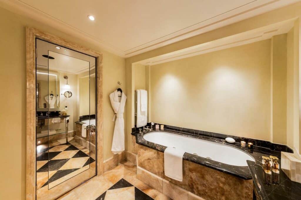Banheira no L'oscar Londres com um espelho, roupão e toalhas ao redor, tudo em mármore, para representar hotéis em Londres