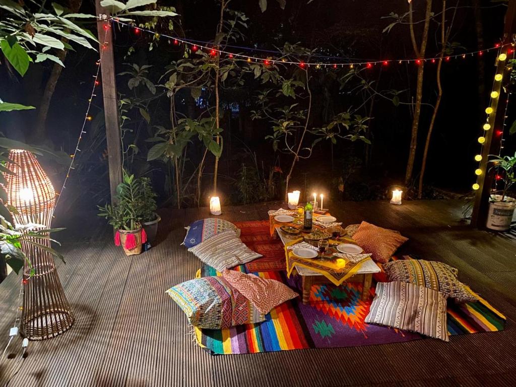Lounge compartilhado na VILA AMZ com almofadas, iluminação indireta, uma mesinha montanha no chão com toalhas coloridas e vasos de flores ao redor