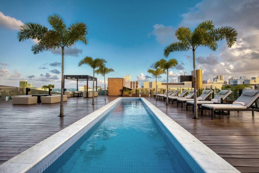 Piscina do LS Hotel com um amplo deck cercado por espreguiçadeiras e coqueiros