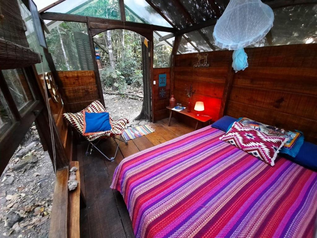 Chalé da Mariri Jungle Lodge no meio da mata, com uma cama de casal, uma poltrona, janelas, abajur e alguns utensílios, tudo bem rústico