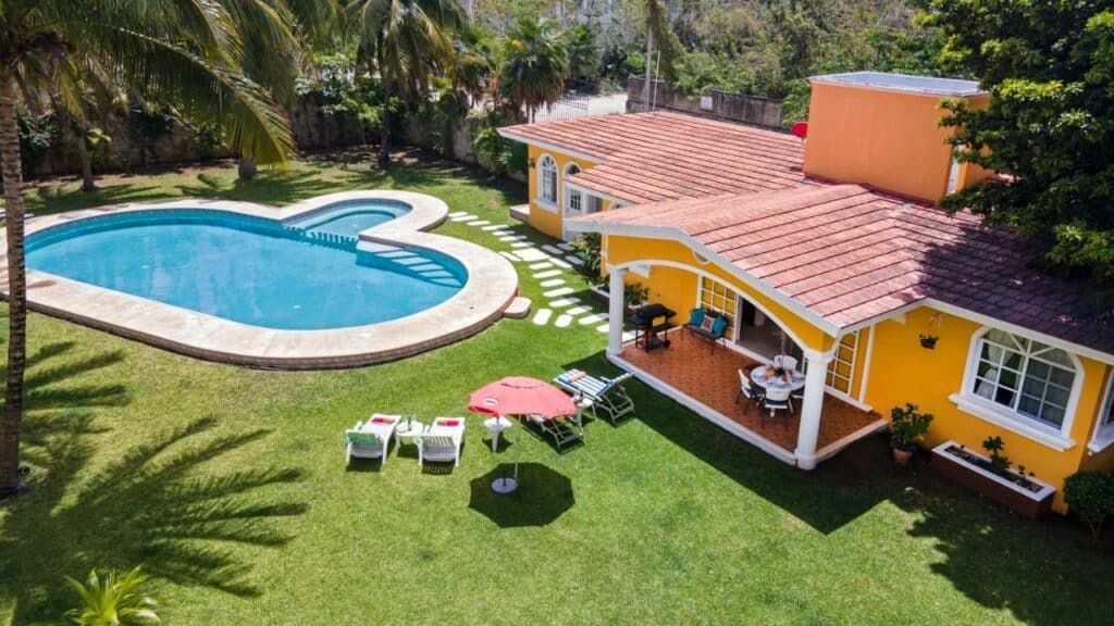 Casa do Orchid's House com uma casa amarela, uma piscina ampla, um extenso gramado, para representar hotéis em Cancun