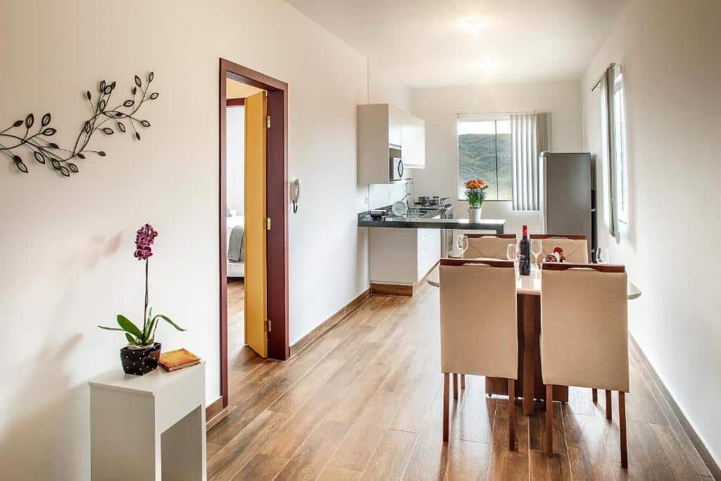 sala de jantar e cozinha do Ouro Preto Apartments com uma mesa e quatro cadeira, uma porta à esquerda com vista para o quarto e um balcão de pedra ao fundo em frente a uma janela com vista para a serra