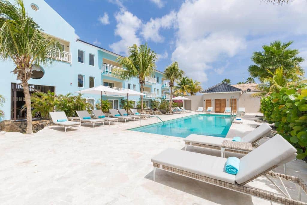 piscina do Dolphin Suites & Wellness Curacao com espreguiçadeiras ao redor  e algumas palmeiras