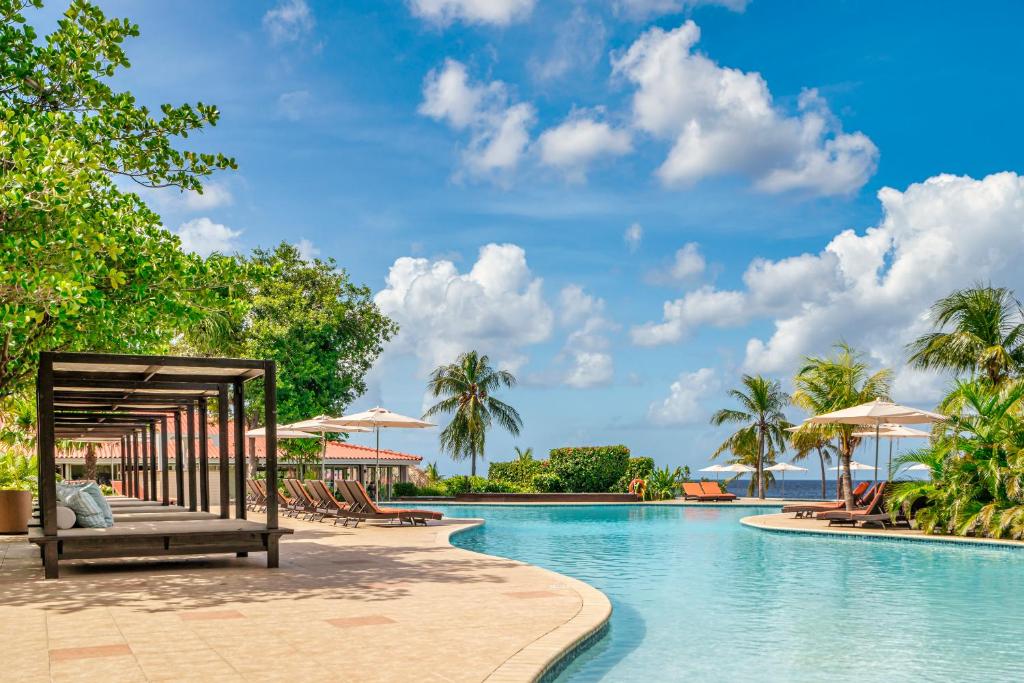 piscina do Dreams Curacao Resort, Spa & Casino em frente ao mar sob um céu azul com nuvens