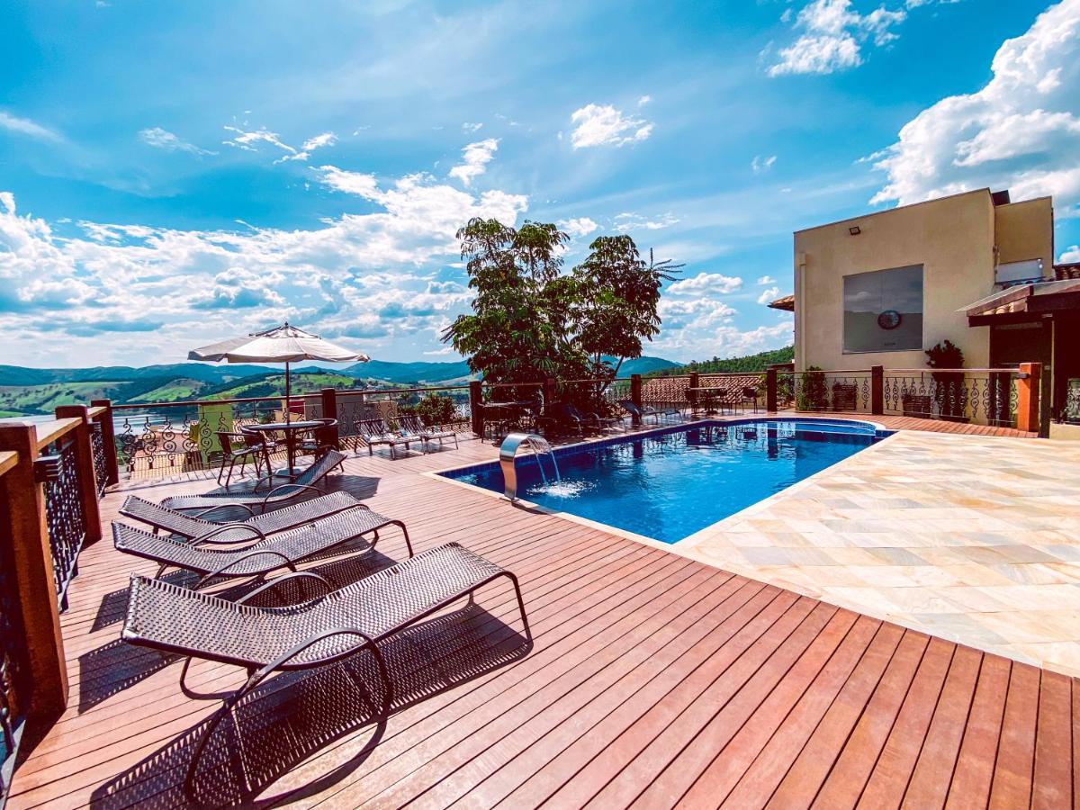 Uma área ensolarada de piscina externa da Pousada Buena Vista com espreguiçadeiras, mesas, guarda-sóis e colinas panorâmicas ao fundo.