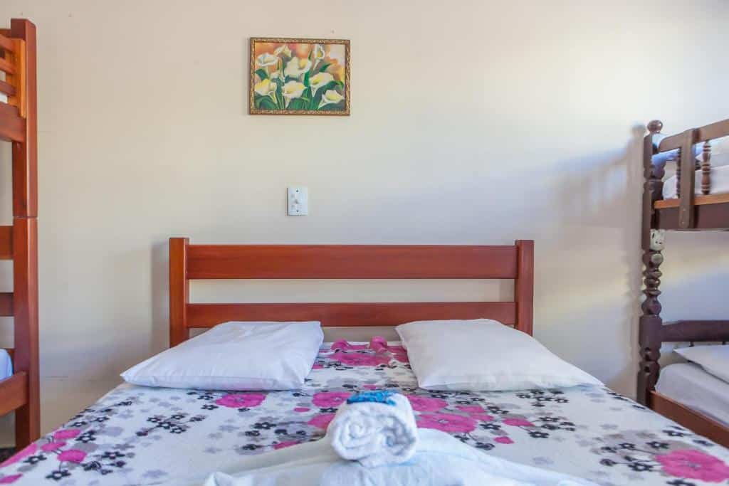 Cama de casal na pousada Caraguá, com duas beliches no mesmo quarto, uma de cada lado da cama