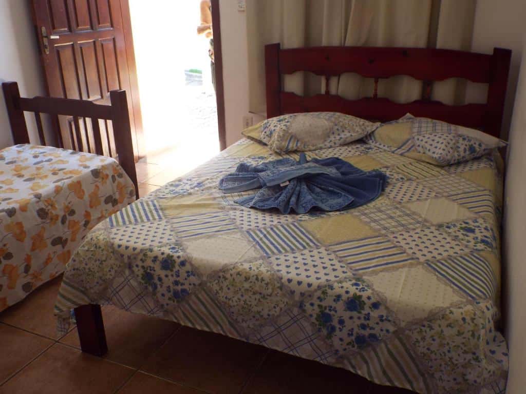 Cama de casal com lençol, travesseiros e toalhas arrumadas, além de uma cama de solteiro bem de frente para a porta