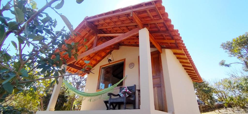 Uma das acomodações da Toca dos Coelhos Carrancas, com uma varanda na frente com uma rede pendurada e uma poltrona com almofada, ao redor, muita natureza