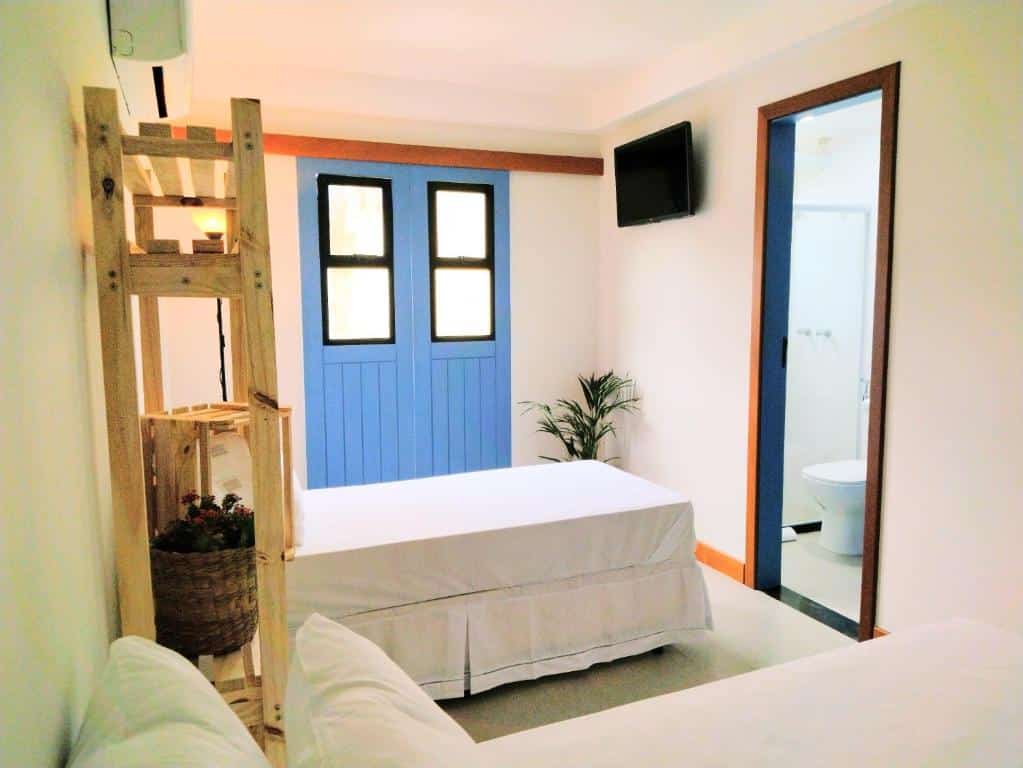 Quarto com banheiro na Pousada VilaZinha, com uma cama de solteiro, um armário aberto de madeira, uma televisão e um vaso de planta