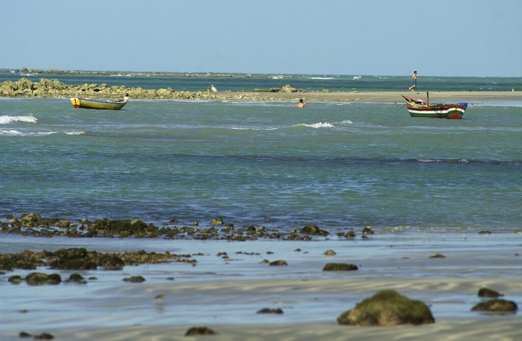 Vista da Praia do Coqueiro com barcos à distâncias e dois homens ao fundo.