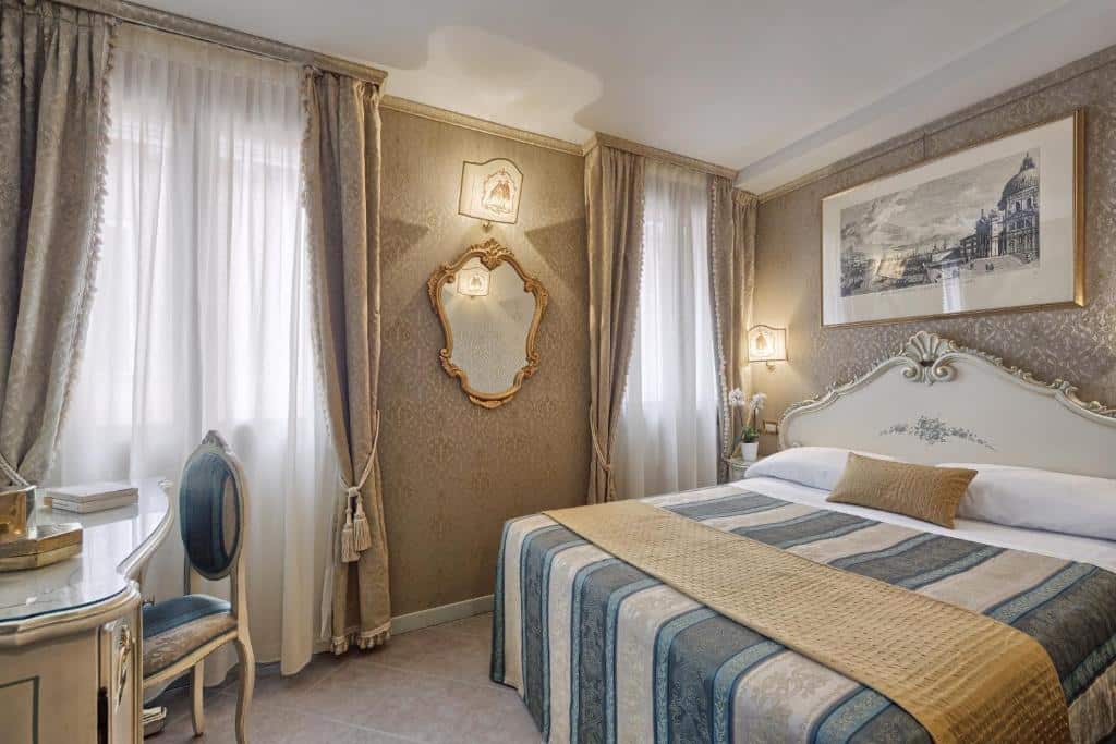Quarto amplo e decorado em estilo renascentista no Antica Locanda al Gambero com uma cama de casal, duas janelas, uma mesa com uma poltrona, um espelho e um quadro, tudo em tons de bege, dourado e azul claro, para representar hotéis em Veneza