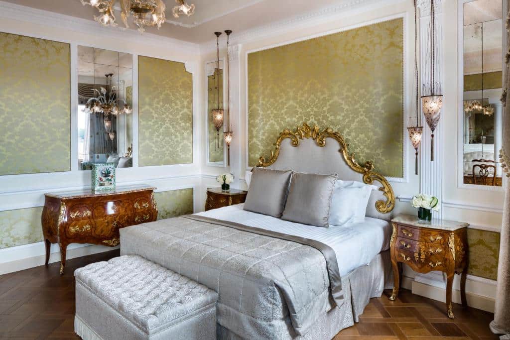 Quarto do Baglioni Hotel Luna, tudo em tons de branco, marrom, dourado e verde claro, a cama é de casal com almofadas e travesseiros, há duas cômodas de estilo renascentista, dois espelhos e algumas luminárias suspensas perto da cama
