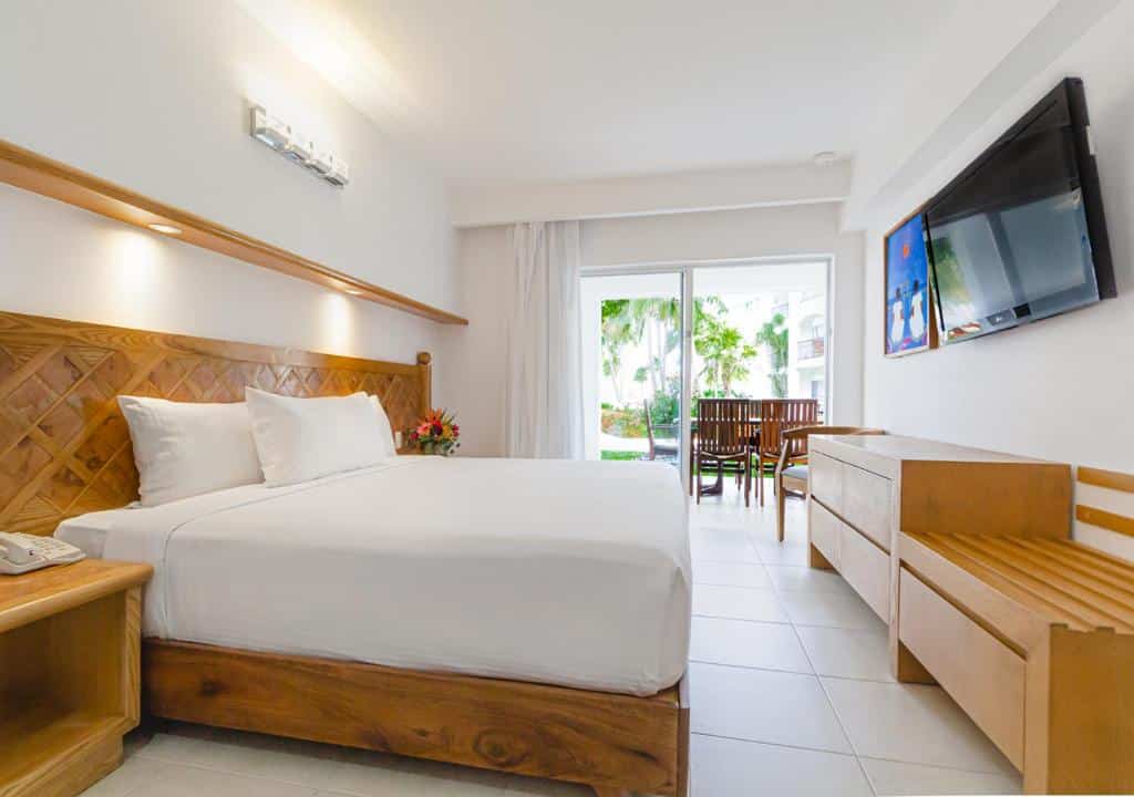 Quarto no Beachscape Kin Ha Villas & Suites com uma varanda extensa com cadeiras, uma cama de casal, uma cômoda e uma televisão, tudo em madeira e as roupas de cama brancas