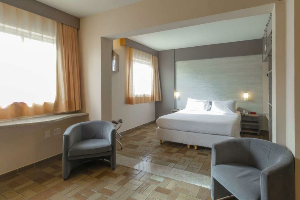 Quarto no Best Western Hotel Caiçara, local amplo, com duas poltronas, uma cama de casal, duas janelas e dois abajures, para representar resorts em João Pessoa