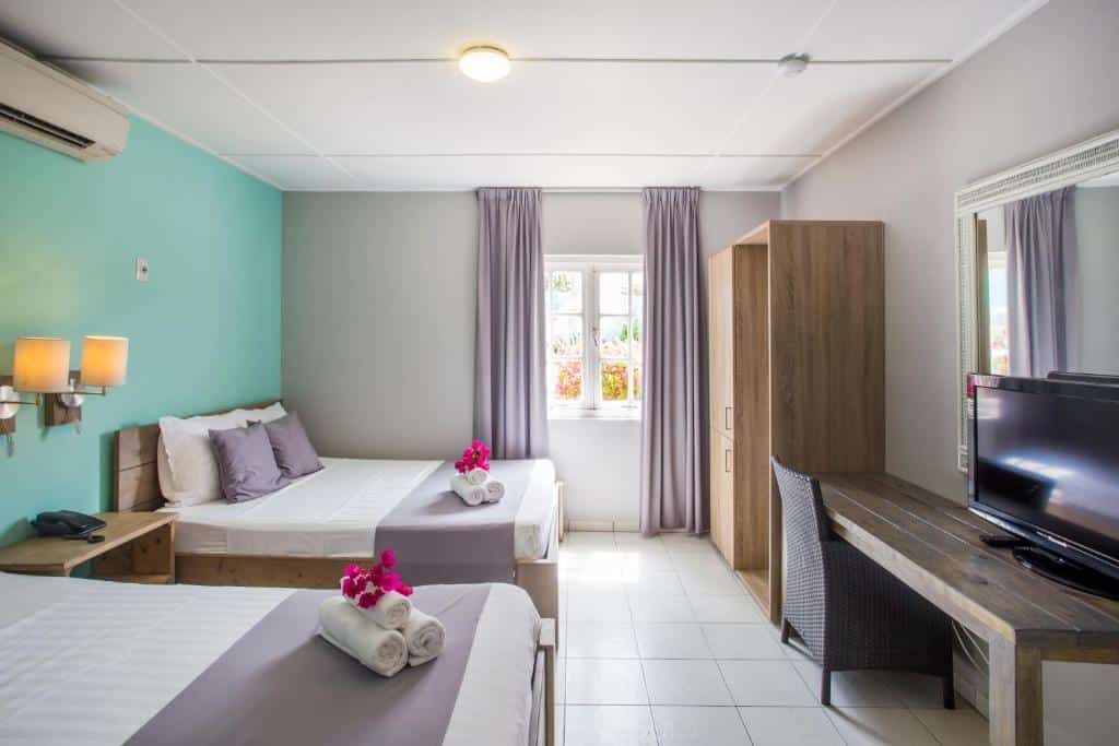 quarto do Bon Bini Seaside Resort Curacao com duas camas de casal, uma mesa com televisão e um ar-condicionado