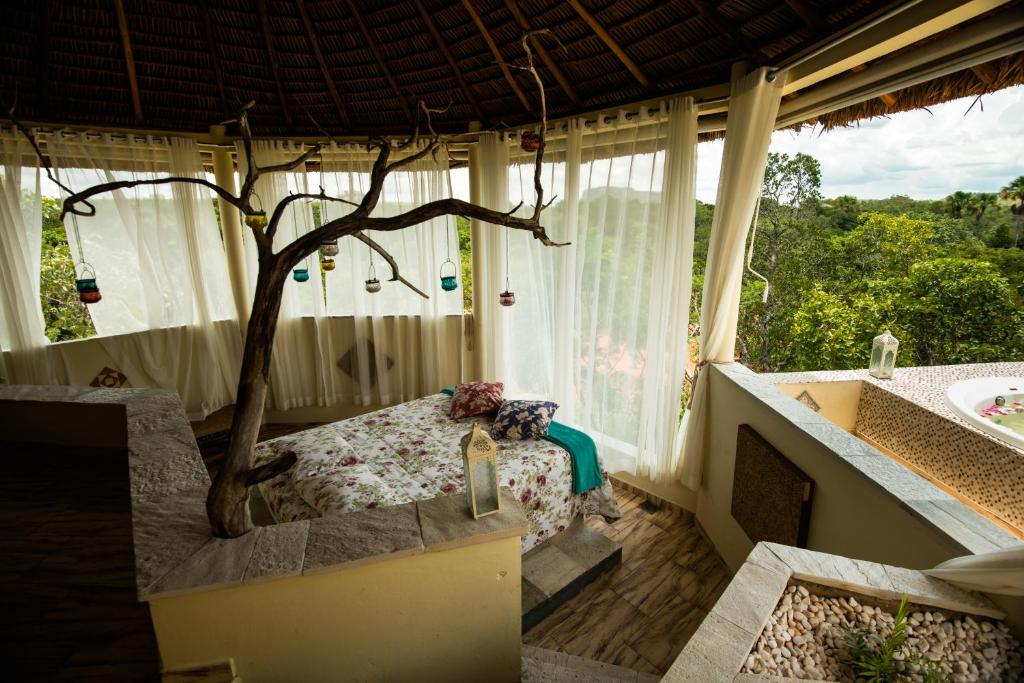 Quarto da Pousada Jalapão Ecolodge com uma cama e um pequeno galho de árvore decorado pendurado perto da cama. Quase todo quarto é aberto, com uma cortina branca e vista de cima para as árvores. Ao lado é possível ver uma banheira redonda.