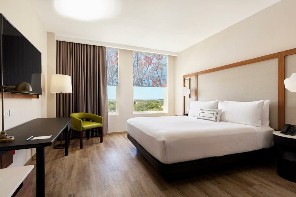 Quarto amplo no Fairfield Inn & Suites by Marriott Cancun Airport com janela dando vista para o jardim, uma cama de casal, uma poltrona, uma luminária de chão, uma mesa e uma televisão