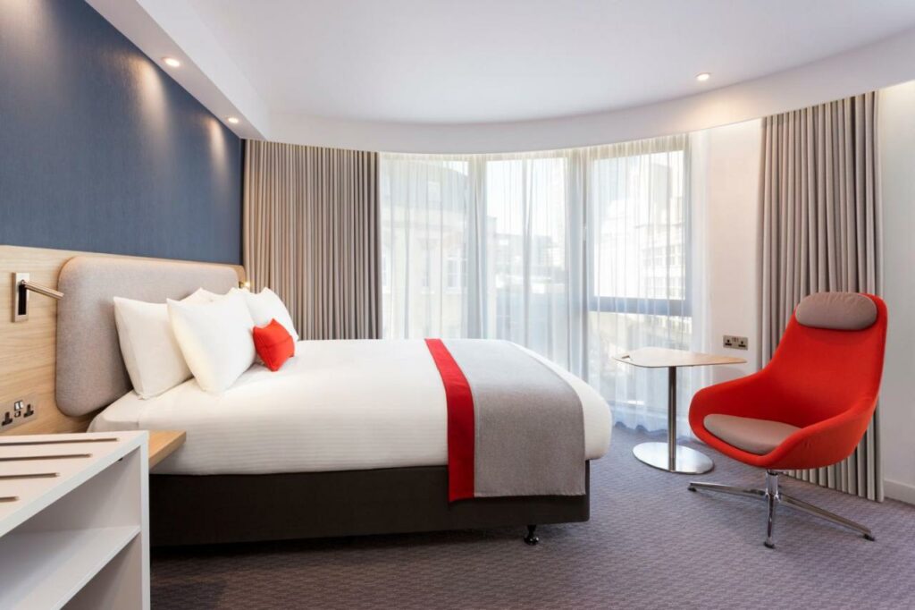 Quarto no Holiday Inn Express Southwark, an IHG Hotel com uma ampla sacada, uma cama de casal, uma poltrona, tudo decorado em tons de azul, vermelho e branco
