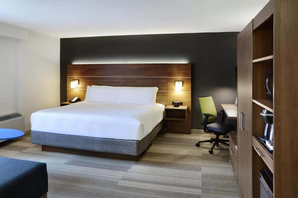 Quarto no Holiday Inn Express Toronto Downtown com um piso de madeira, uma cama de casal, uma mesa de escritório com cadeira, cabeceira com abajures e um armário, para hotéis em Toronto