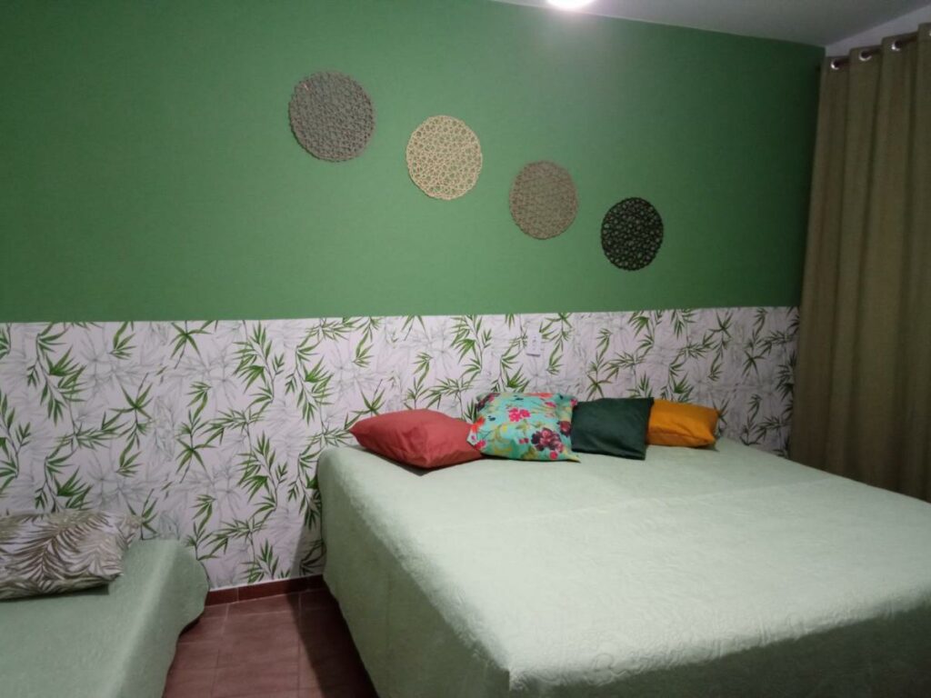 Quarto na Hospedaria Vila Else, uma cama de casal e uma de solteiro, com almofadas coloridas, tudo decorado em tons de verde e branco